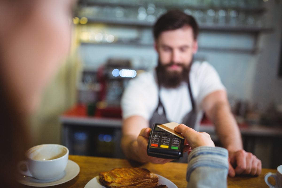Un camarero cobra un desayuno con datáfono a un cliente