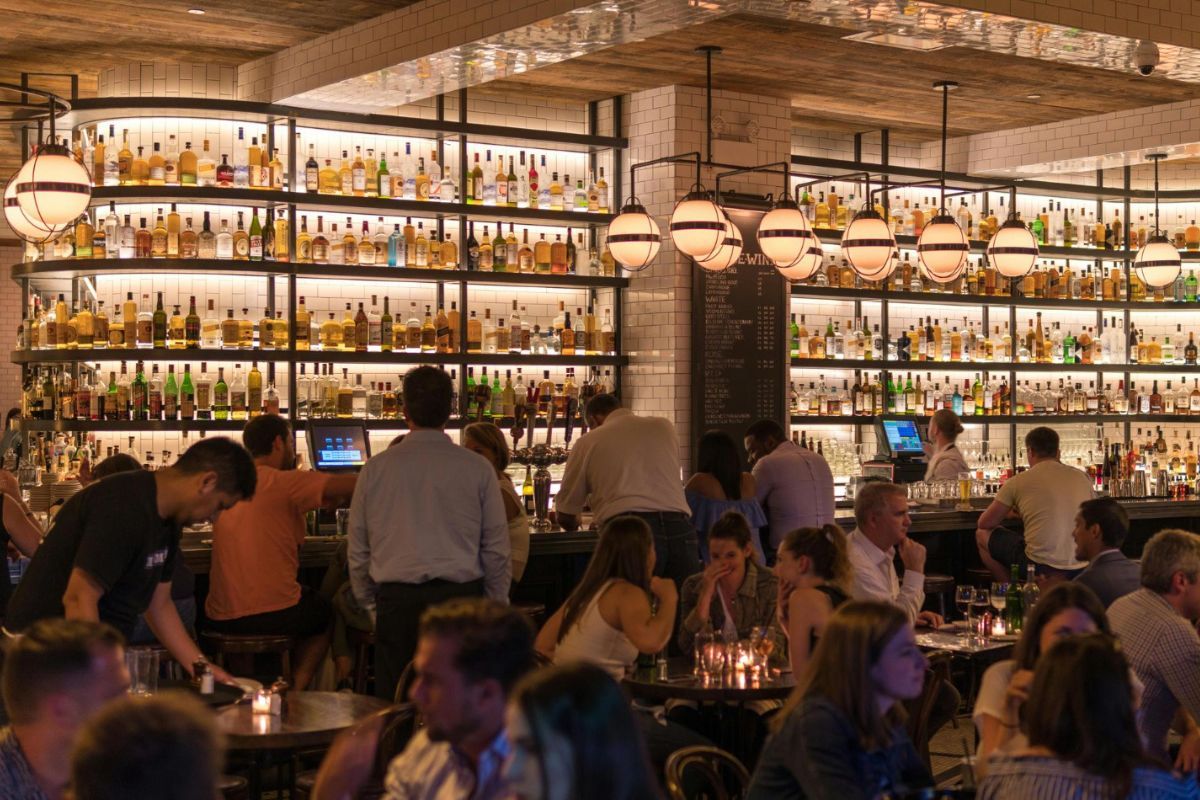 Un bar moderno con barra y mesas lleno de clientes 
