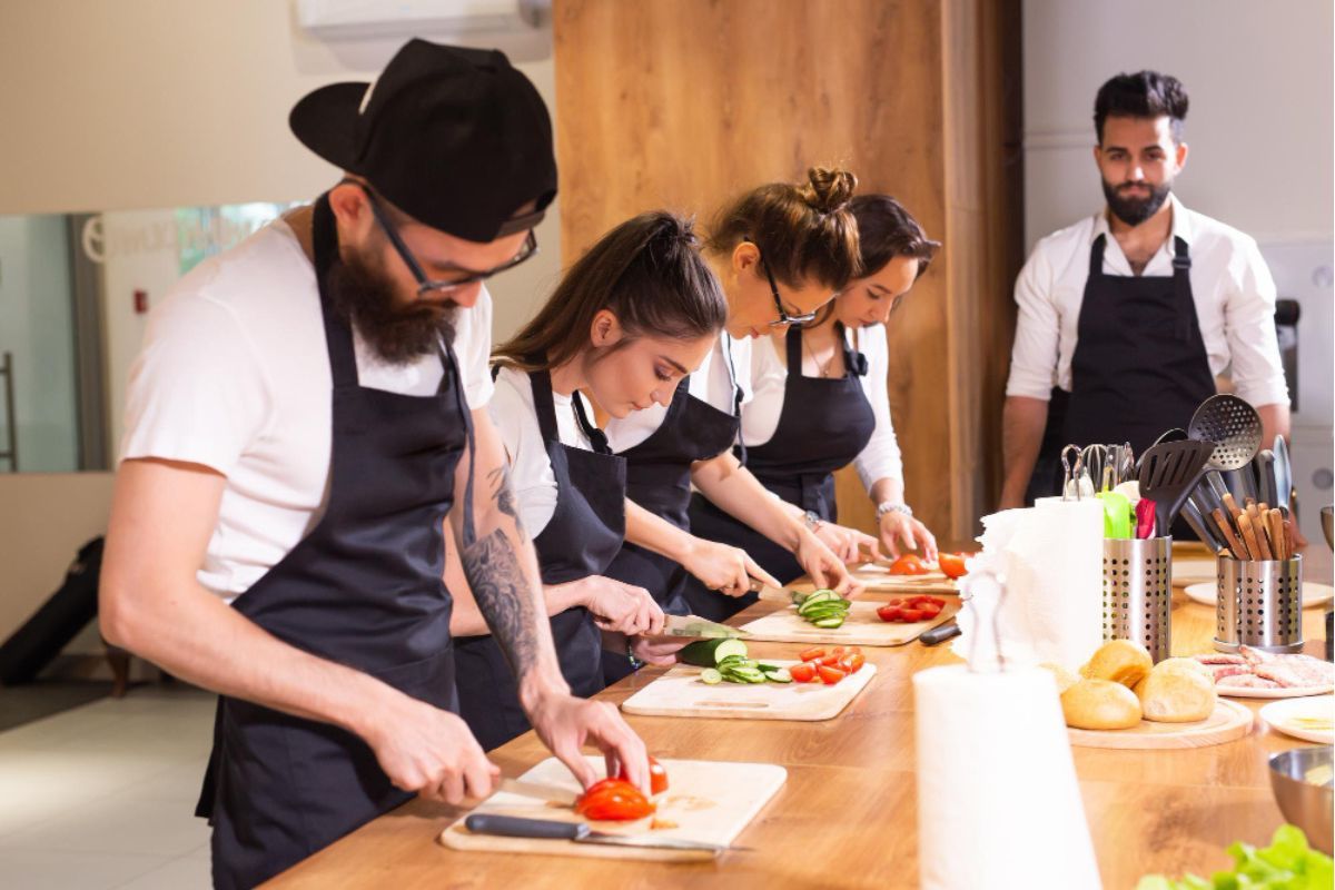 Cuatro alumnos practican corte de verduras supervisados por un profesor