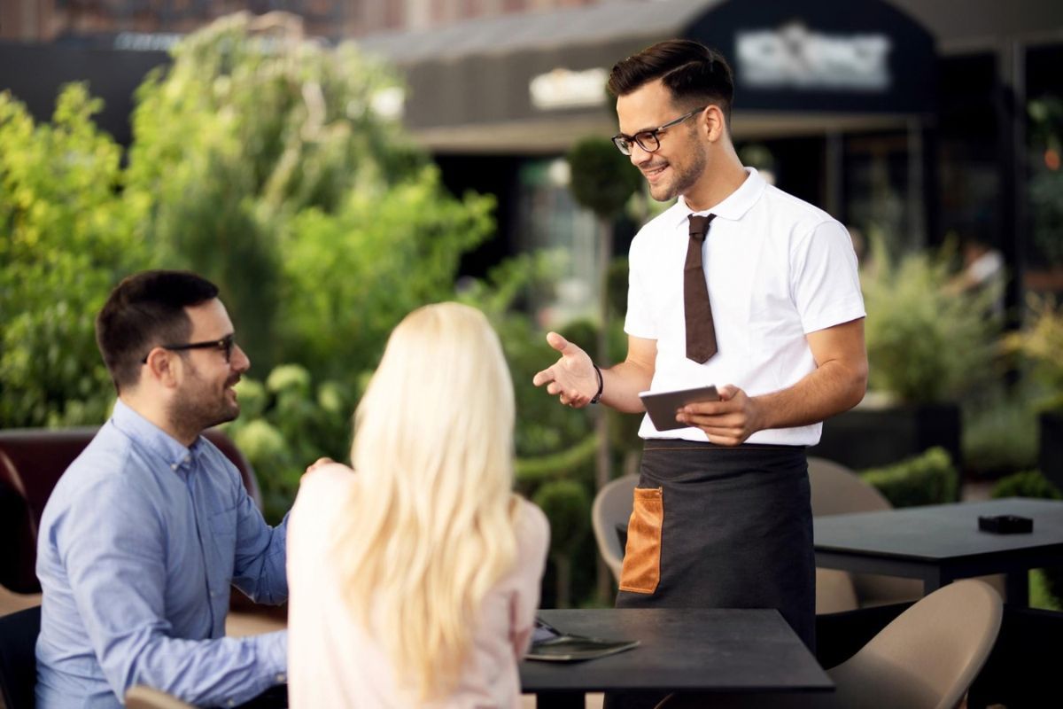 Camarero aconseja a dos clientes sentados en una terraza