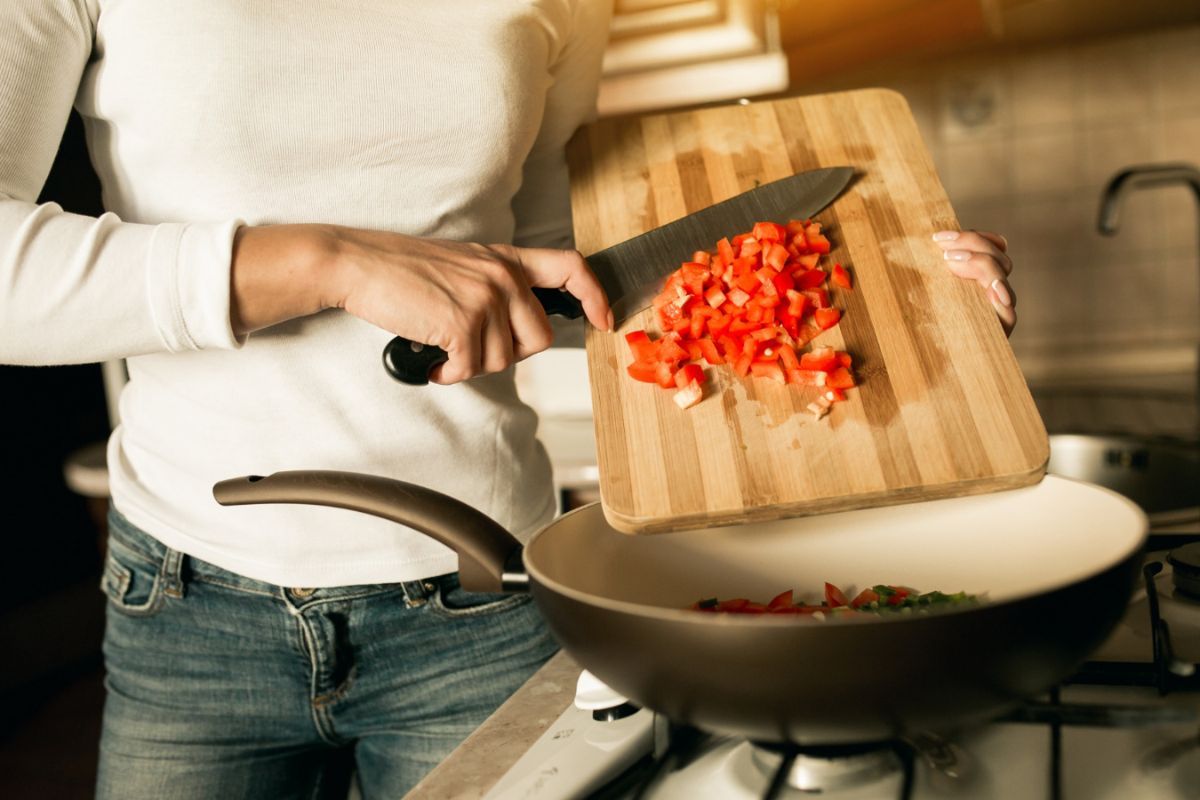 Una mujer echa tomate cortado en pedazos desde una tabla de madera a una sartén