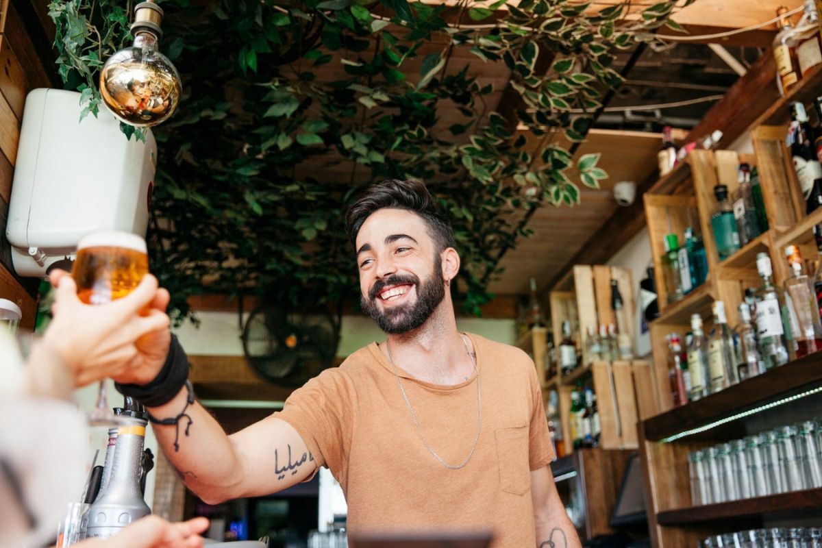 Un camarero sonriente entrega una cerveza a un cliente