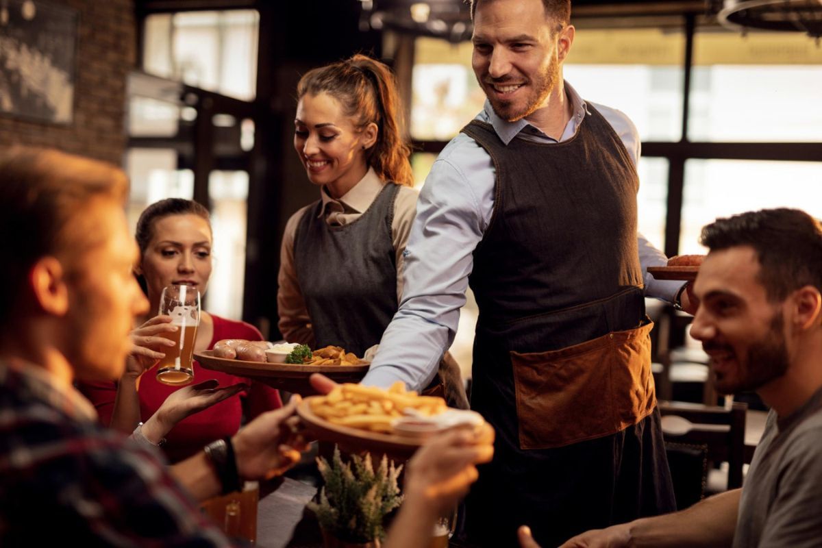  Dos camareros sirven platos de comida a una mesa en la que hay varios comensales