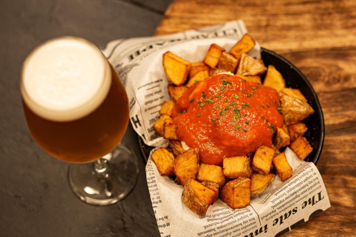 cerveza en copa junto a una ración de patatas bravas en una mesa de un bar